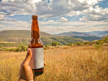 Midsection of man holding glass bottle against sky