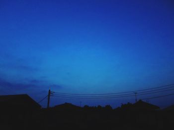 Low angle view of silhouette electricity pylons against clear blue sky