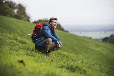 Smiling mature man crouching on grass