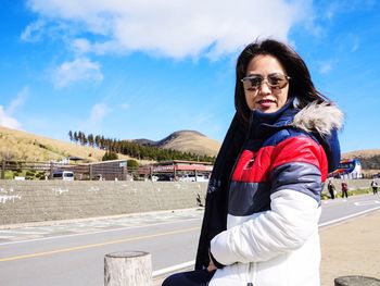 Portrait of smiling young woman standing by mountain against sky