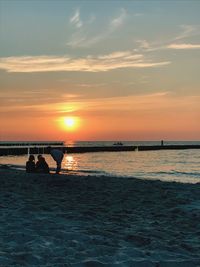 Silhouette people on beach against sky during sunset