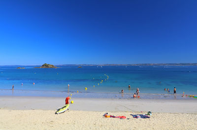 People at beach against clear blue sky