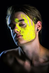 Close-up of teenage boy with yellow face paint against black background