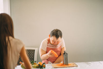 Lifestyle, education. an elderly woman with down syndrome rubs carrots on a grater with an assistant