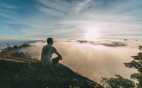 Side view of man standing on rock against sky