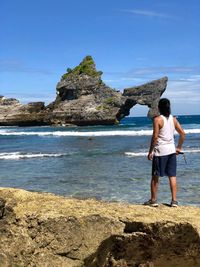 Rear view of woman standing on rock by sea