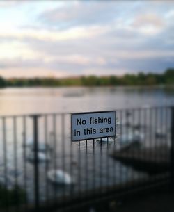 Close-up of sign by river against sky