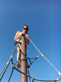 Low angle view of woman standing on outdoor play equipment against clear blue sky