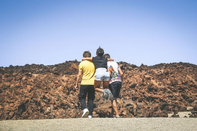 Rear view of playful family on land against clear blue sky