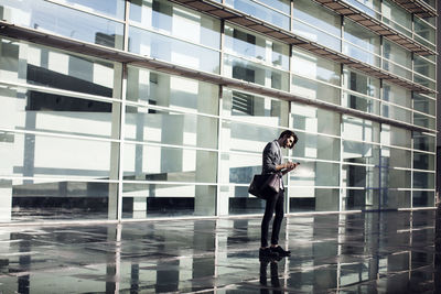 Businessman carrying bag and using mobile phone while standing office