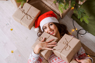 Happy excited young woman in santa claus hat with gift box at home on floor