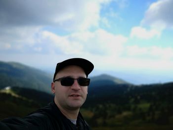 Portrait of mid adult man wearing sunglasses standing on mountain against sky