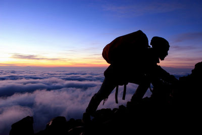 Man climbing on mountain against sky during sunset