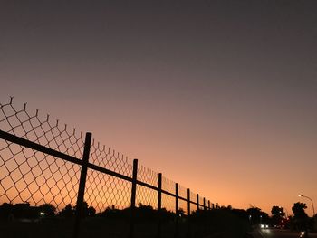 Silhouette fence against sky during sunset