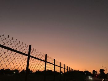 Silhouette fence against sky during sunset