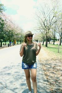 Portrait of smiling woman showing thumbs up while standing on road 