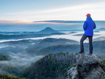 Man on the mountain peak looking on long valley with heavy mist at colorful sunset in early autumn