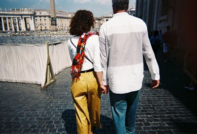 Rear view of couple walking on footpath in city