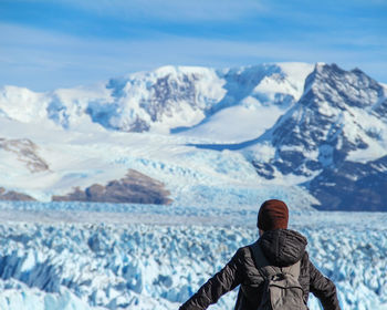 Rear view of man standing on snowcapped mountains against sky