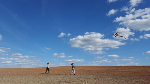 People flying kite while standing on ground against sky