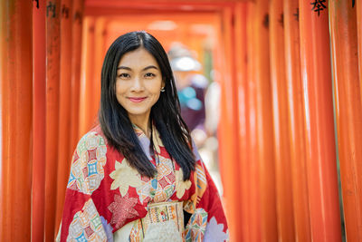 Portrait of smiling young woman standing against wall