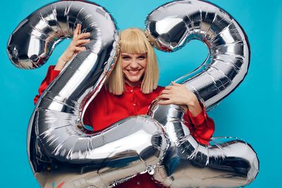 Portrait of smiling young woman with balloons against wall