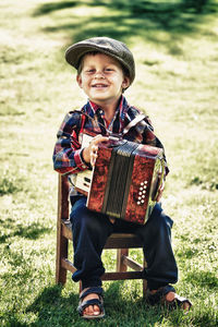 Full length portrait of boy holding accordion while sitting on chair at land