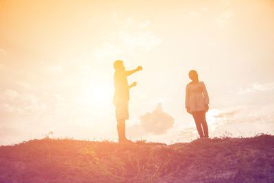 Rear view of friends standing on field against sky during sunset