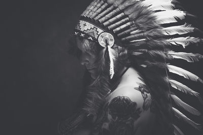 Side view of naked fashion model wearing war bonnet against black background