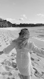 Rear view of woman standing at beach against sky