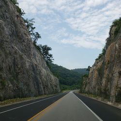 Empty road along trees and mountains against sky