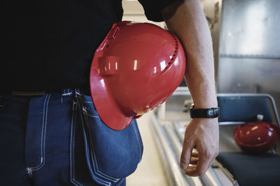 Midsection of auto mechanic teacher with red hardhat while standing at workshop