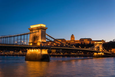 Illuminated chain bridge over danube river against clear blue sky at night