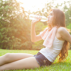 Young woman drinking water from while sitting on grass