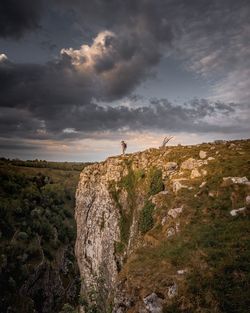 Person standing on cliff against cloudy sky