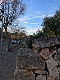 Stone wall by rocks and trees against sky