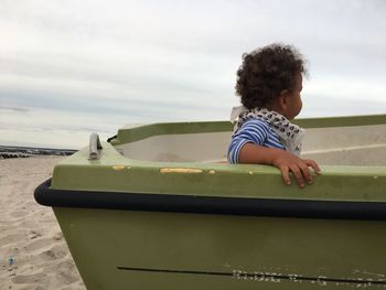 Side view of cute baby boy sitting on boat at beach against sky