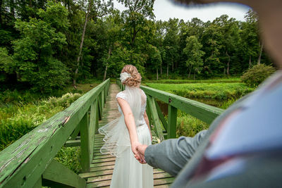 People standing on footbridge amidst trees against sky