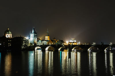 Illuminated buildings by river against sky at night