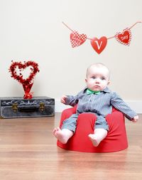 Toddler wearing bow tie sitting on floor seat at home during valentine day