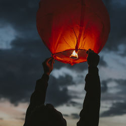 Person holding red lantern against sky during sunset