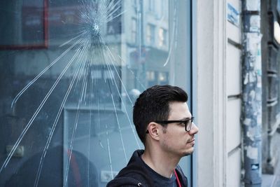 Man looking away while standing by cracked window glass