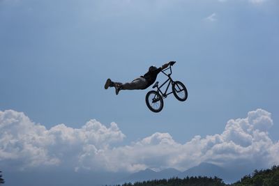 Low angle view of man with bicycle performing stunt against sky during sunny day