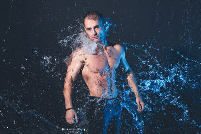 Portrait of shirtless man standing against black background