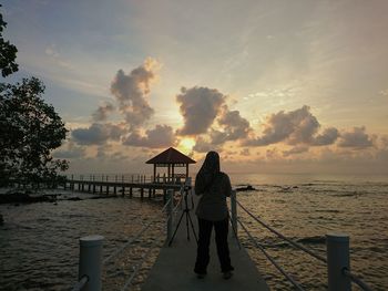 Rear view of silhouette man by sea against sky during sunset