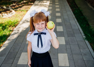 Back to school. a little schoolgirl stands in the school yard and holds an apple in her hands.