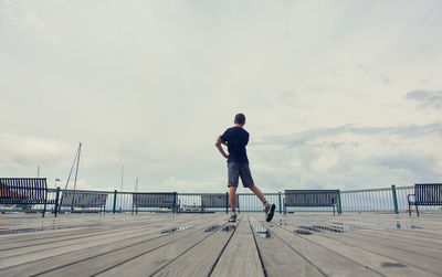 Rear view of man standing on pier against sky