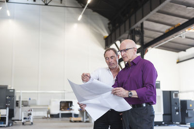 Two businessmen looking at plan in factory shop floor