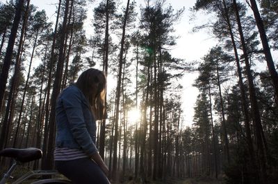 Woman sitting on bicycle against trees at forest