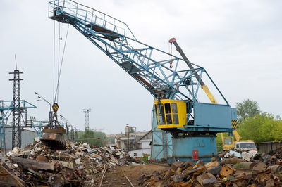 Crane at metallic junkyard against sky